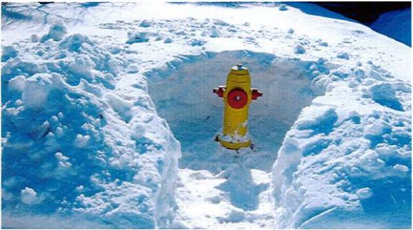 Image of a yellow fire hydrant in winter surrounding by a snow drift almost as tall as the hydrant. The snow around the hydrant has been cleared to allow 1.5m of access around it.
