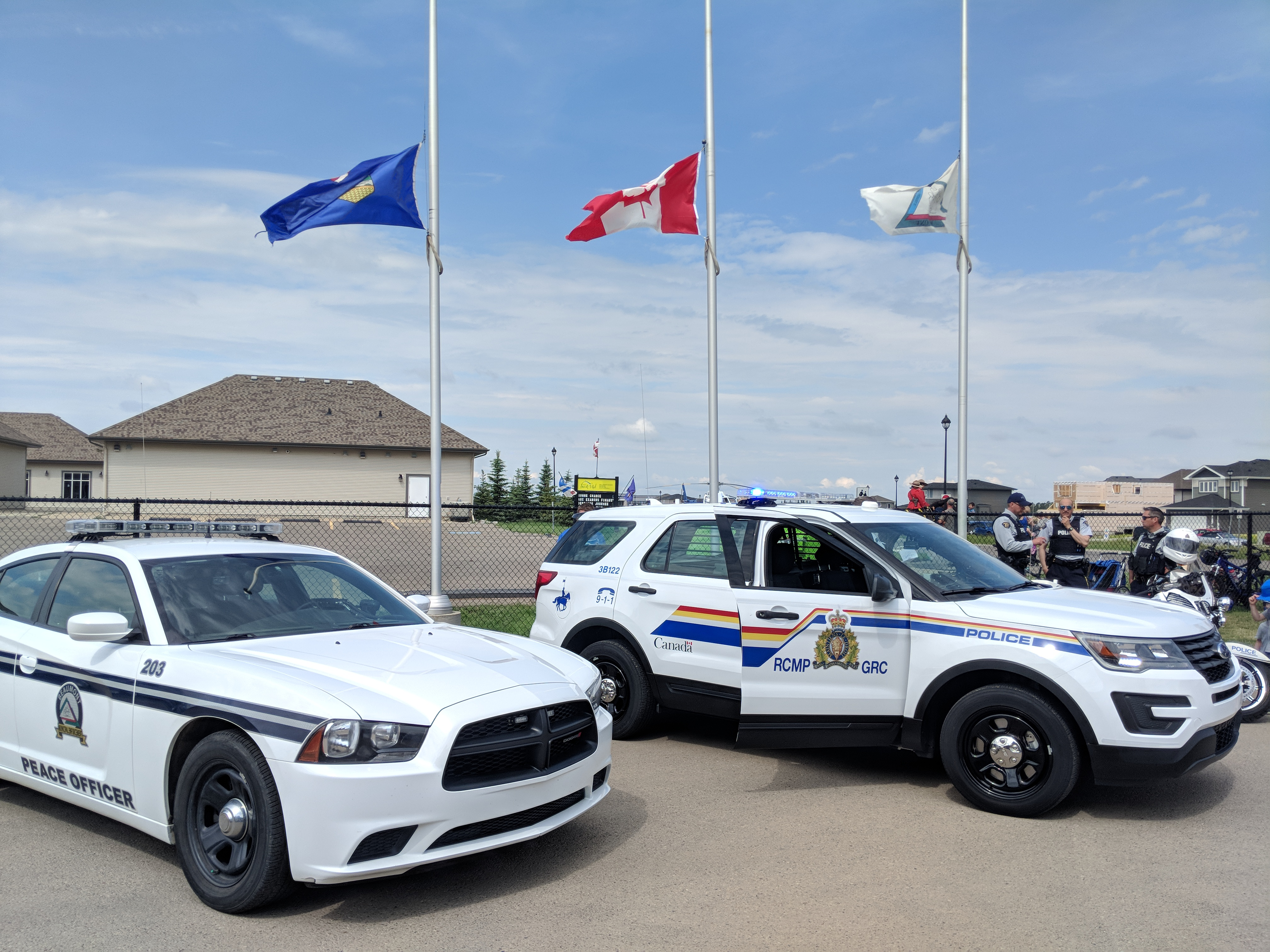 Photo of two RCMP vehicles parked in front of three flag poles with flags flying half-mast.