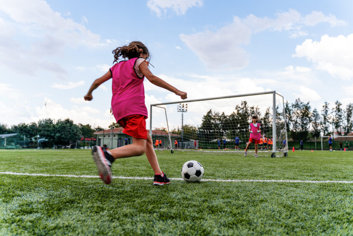 Child playing soccer in an outdoor field.