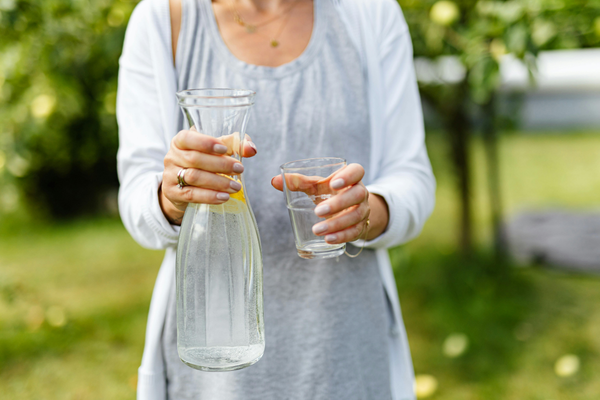 Woman holding a glass of water and water pitcher with lemon slices